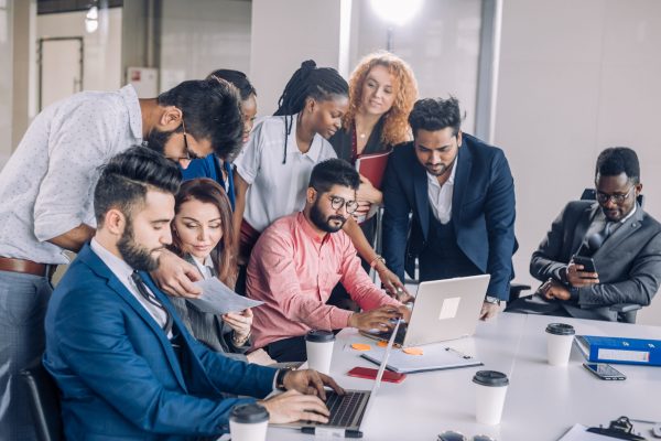 Woman showing coworkers something on laptop computer as they gather around a conference table